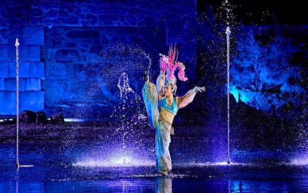 Performer in colorful costume dancing amid water fountains at Puy du Fou España night show.