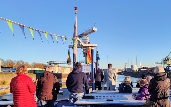 Tourists on a boat during a Cologne Harbour tour, with industrial cranes and containers in the background.