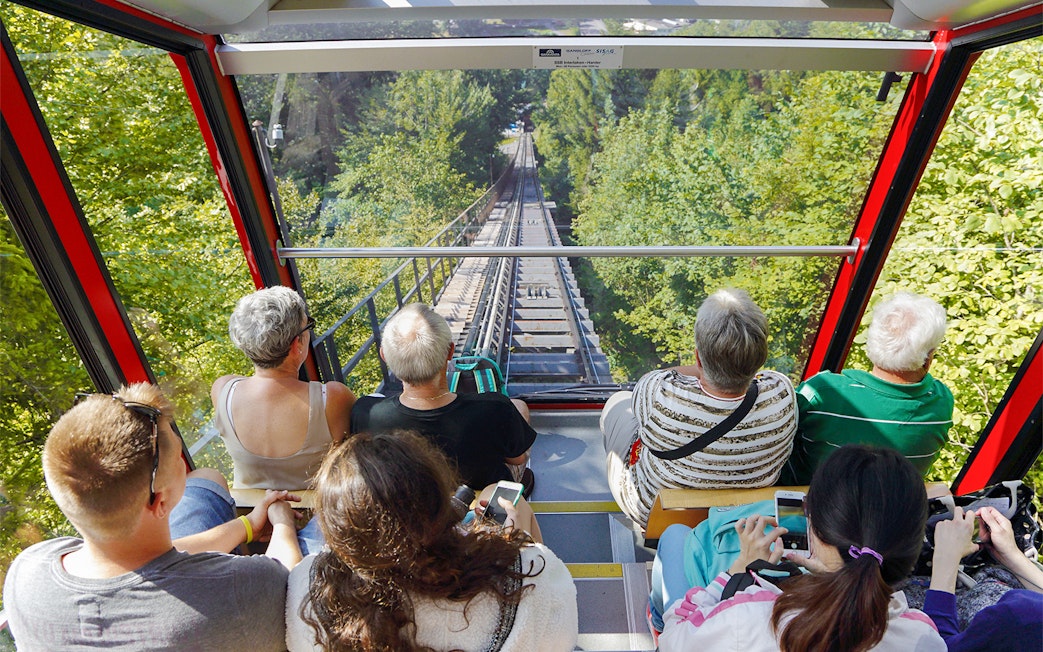 View from inside Harder Kulm funicular train, passengers looking at forested track.