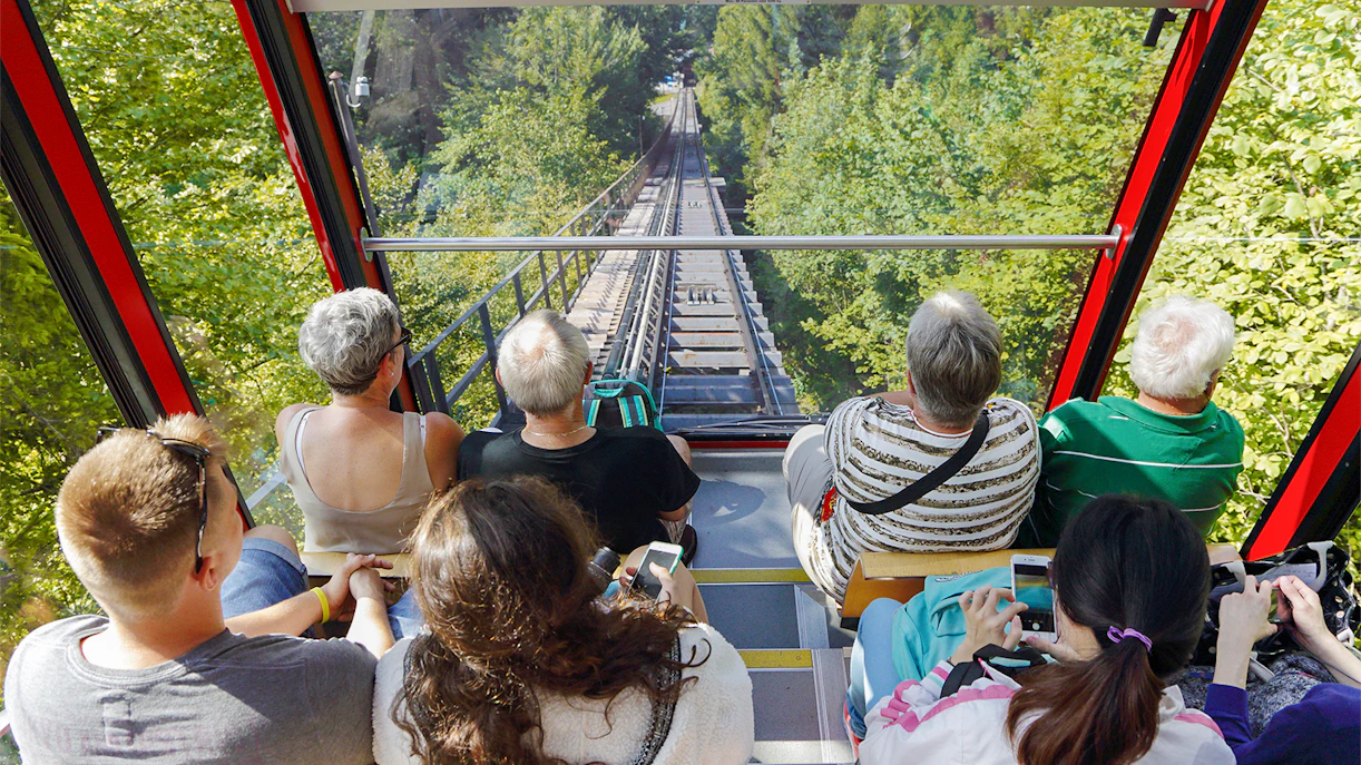 View from inside Harder Kulm funicular train, passengers looking at forested track.