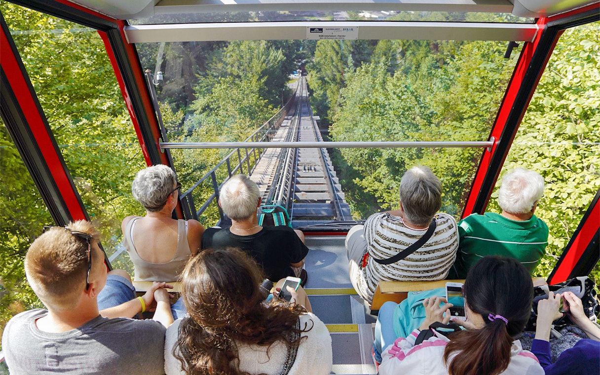 View from inside Harder Kulm funicular train, passengers looking at forested track.