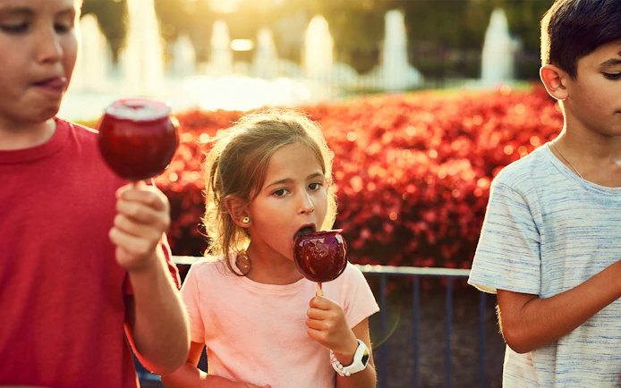 Children enjoying candied apples at Canada's Wonderland with fountains in the background.
