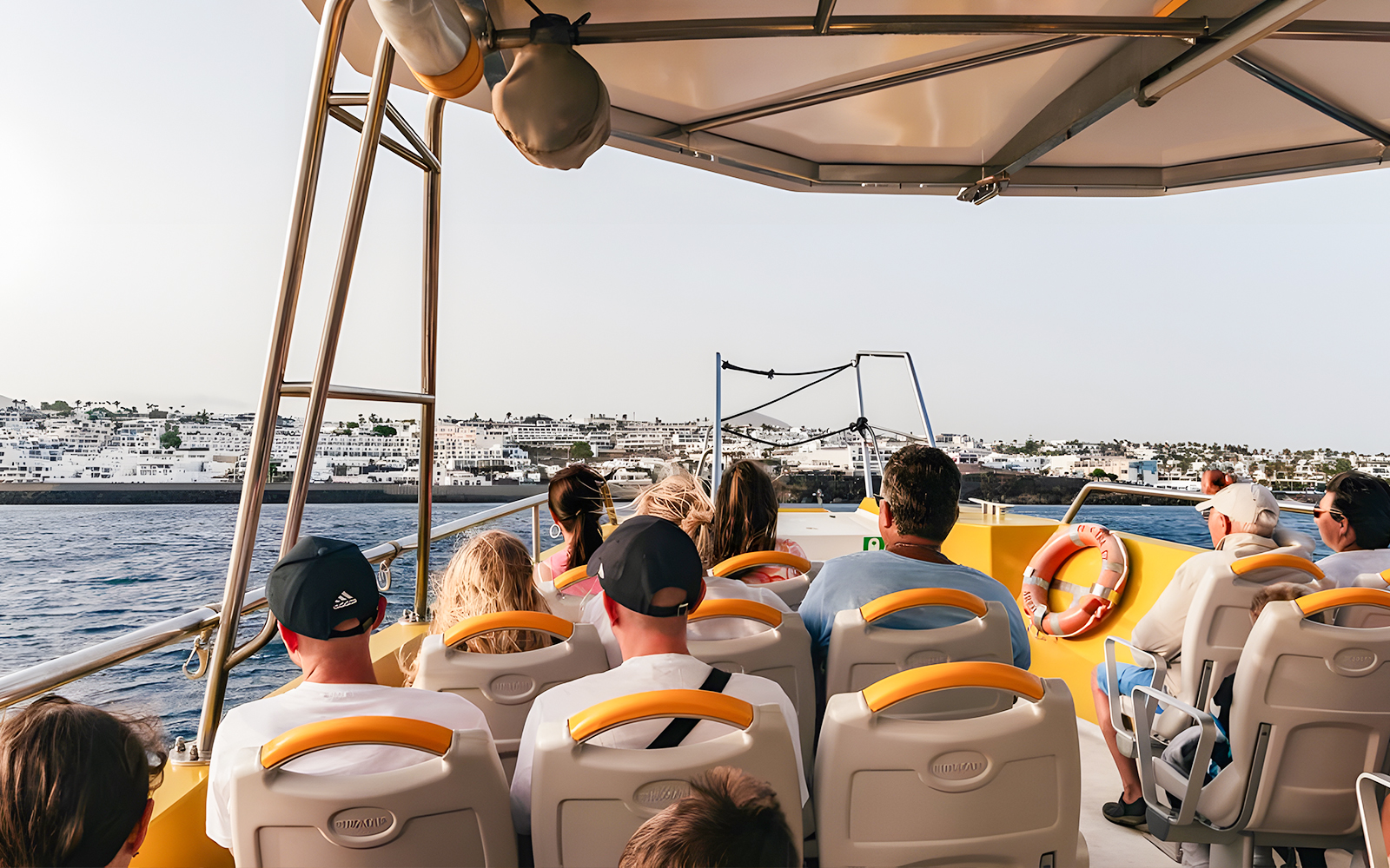 Tourists seated inside a speedboat during a sunset dolphin cruise near coastal buildings.