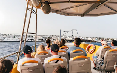 Tourists seated inside a speedboat during a sunset dolphin cruise near coastal buildings.