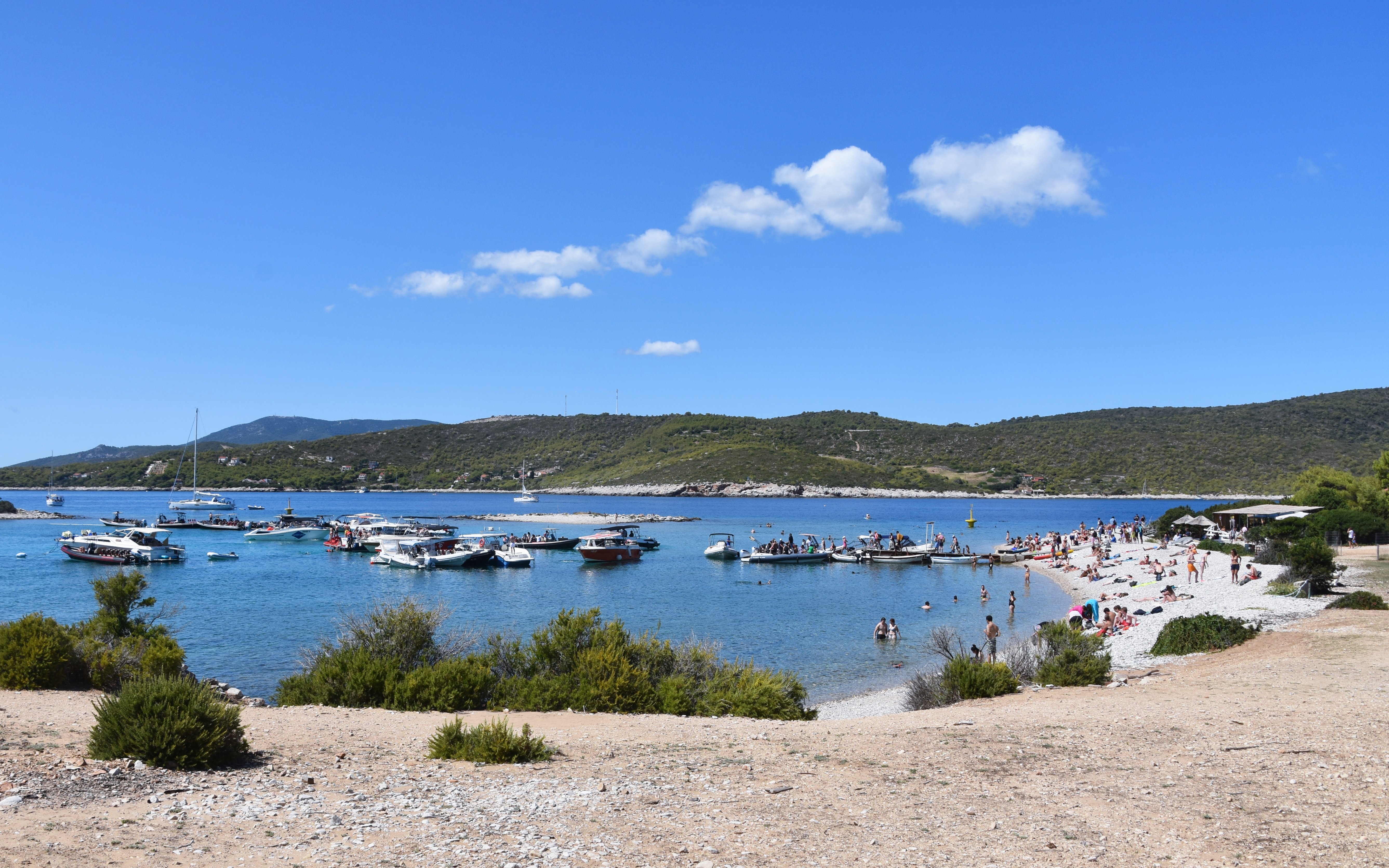 Boats anchored near Budikovac Island's Blue Lagoon, Croatia, with people swimming and relaxing on the beach.