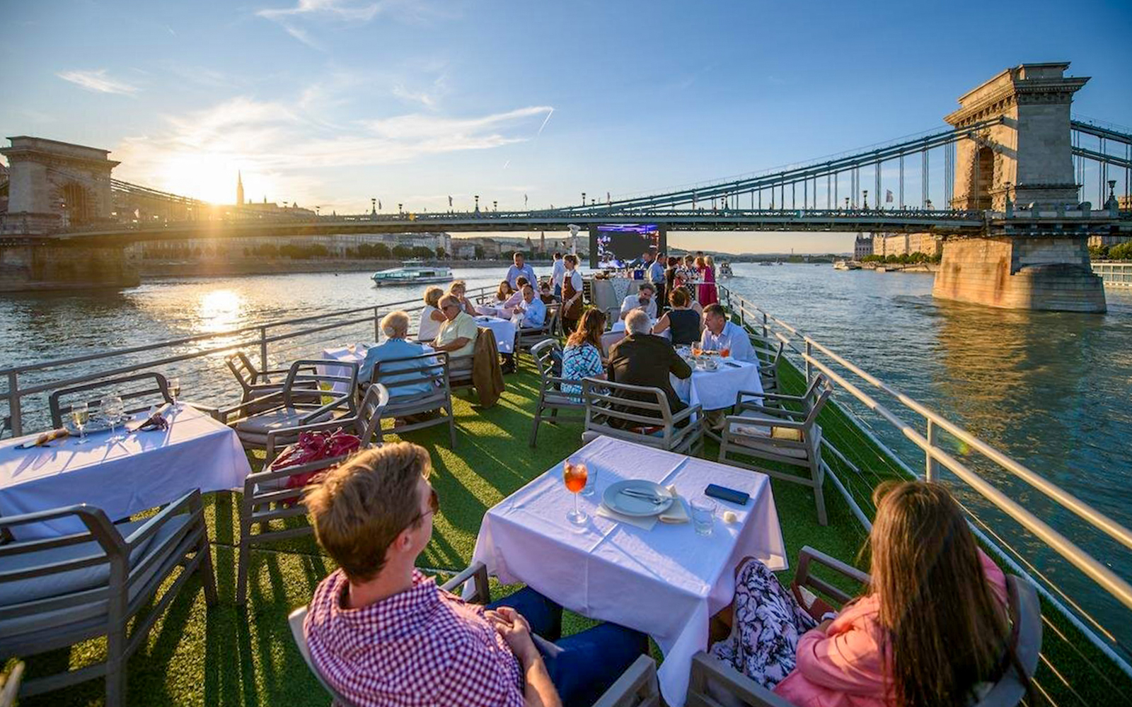 Guests on a Budapest Danube River cruise enjoying drinks with a view of the Chain Bridge at sunset.
