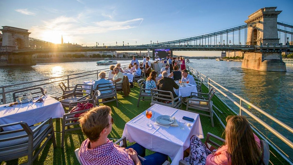 Guests on a Budapest Danube River cruise enjoying drinks with a view of the Chain Bridge at sunset.