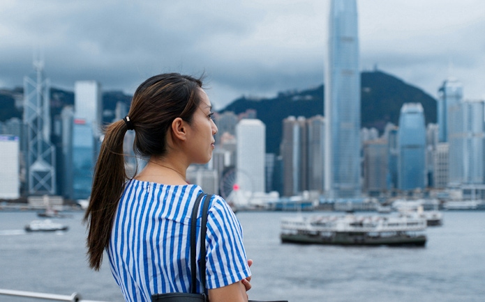 Woman overlooking Hong Kong skyline with ferries on Victoria Harbour.