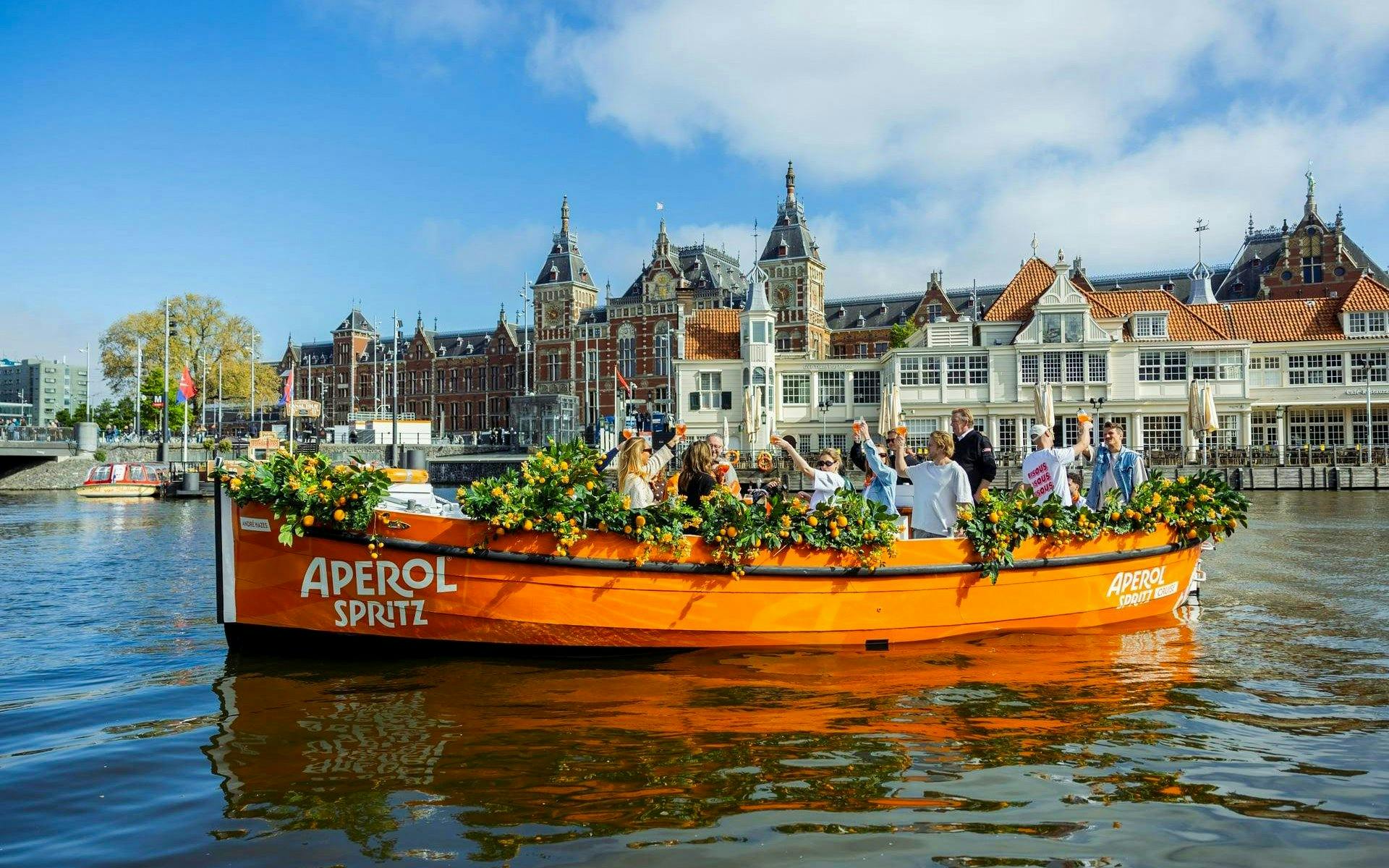 Guests enjoying Aperol Spritz Cruise on a decorated boat in Amsterdam canal.