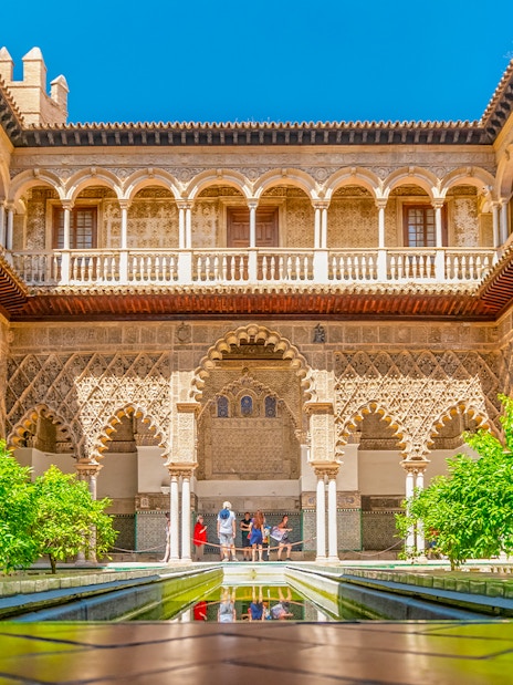 Moorish arches and courtyard of Real Alcazar, Seville, with lush greenery.