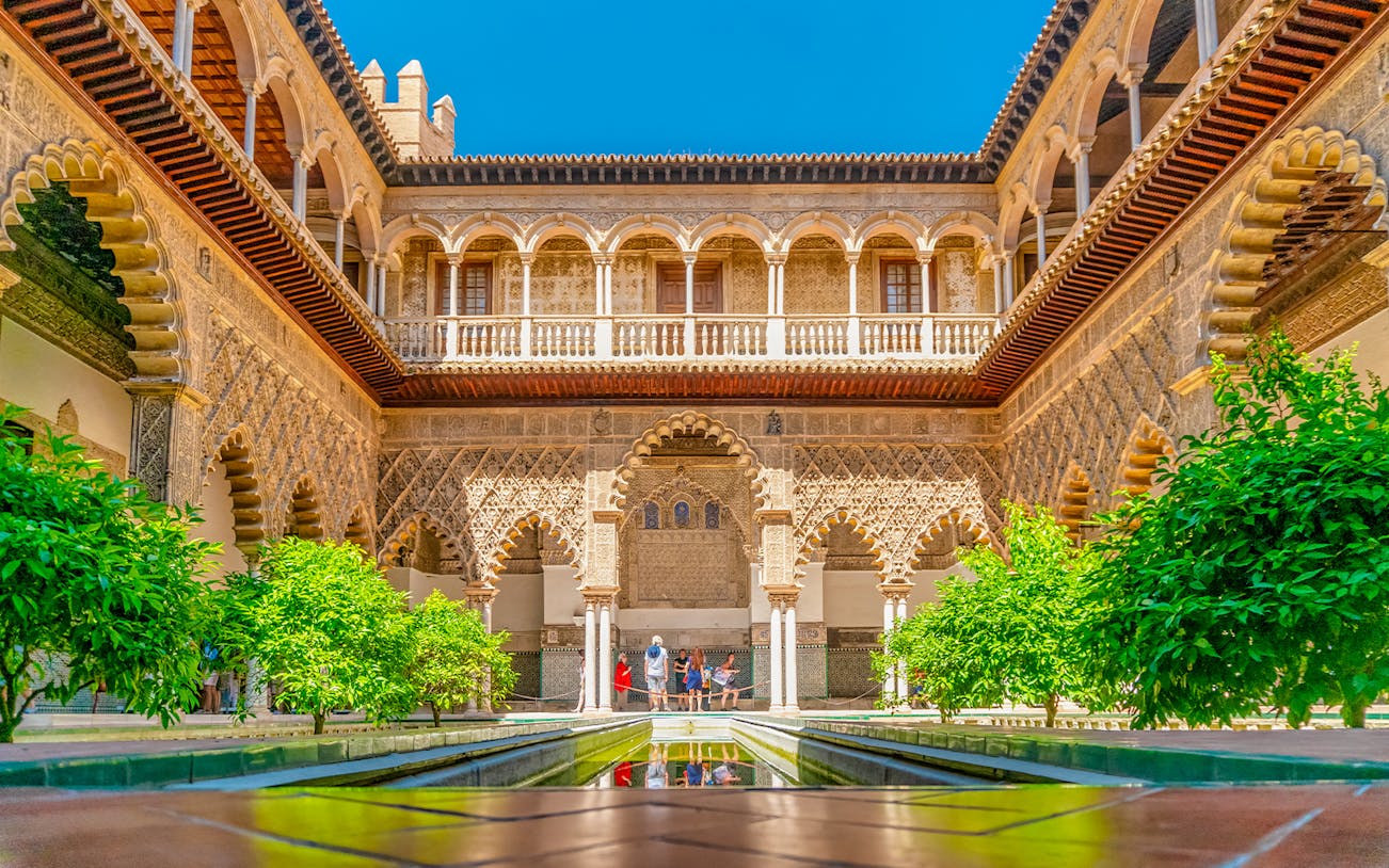 Moorish arches and courtyard of Real Alcazar, Seville, with lush greenery.