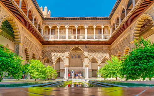 Moorish arches and courtyard of Real Alcazar, Seville, with lush greenery.