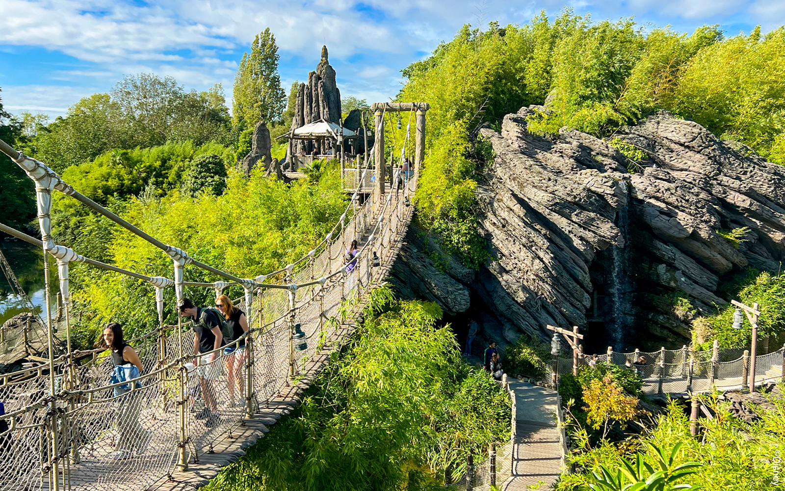 Suspension bridge over lush greenery at Adventure Isle, Disneyland Paris Park.