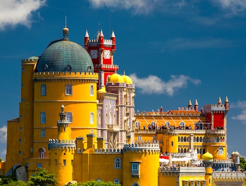 Pena Palace in Sintra, Portugal, with vibrant yellow and red towers against a blue sky.