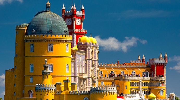 Pena Palace in Sintra, Portugal, with vibrant yellow and red towers against a blue sky.