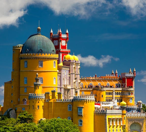 Pena Palace in Sintra, Portugal, with vibrant yellow and red towers against a blue sky.