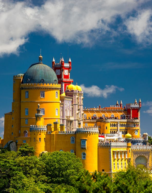 Pena Palace in Sintra, Portugal, with vibrant yellow and red towers against a blue sky.