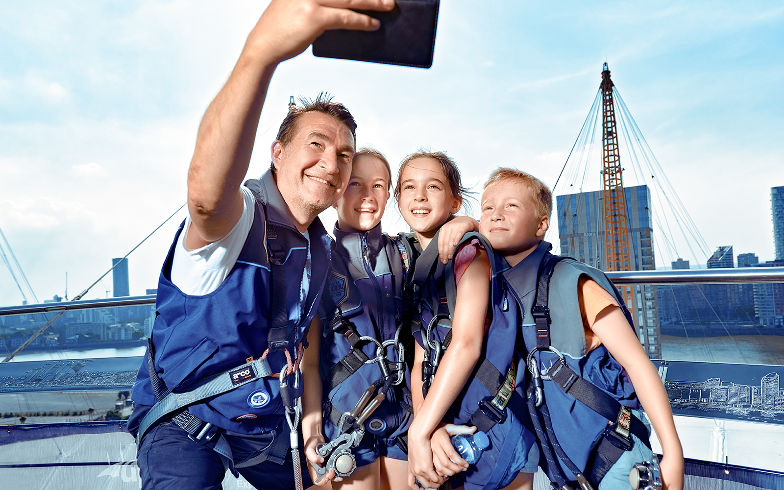 Visitors taking a selfie on the roof of The O2 in London, wearing climbing gear.