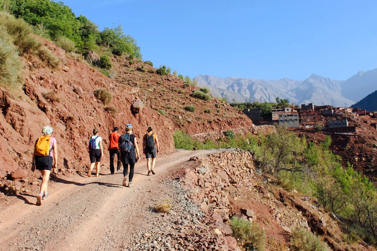 Group hiking on a rocky trail towards Tamsoult Waterfall, Ouirgane, with Atlas Mountains in view.