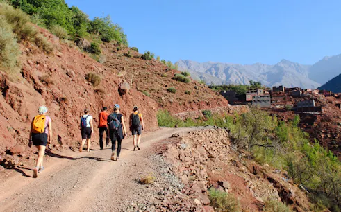 Group hiking on a rocky trail towards Tamsoult Waterfall, Ouirgane, with Atlas Mountains in view.