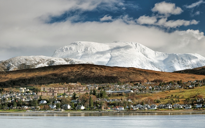 Fort William town with snow-covered Ben Nevis in the background during winter.