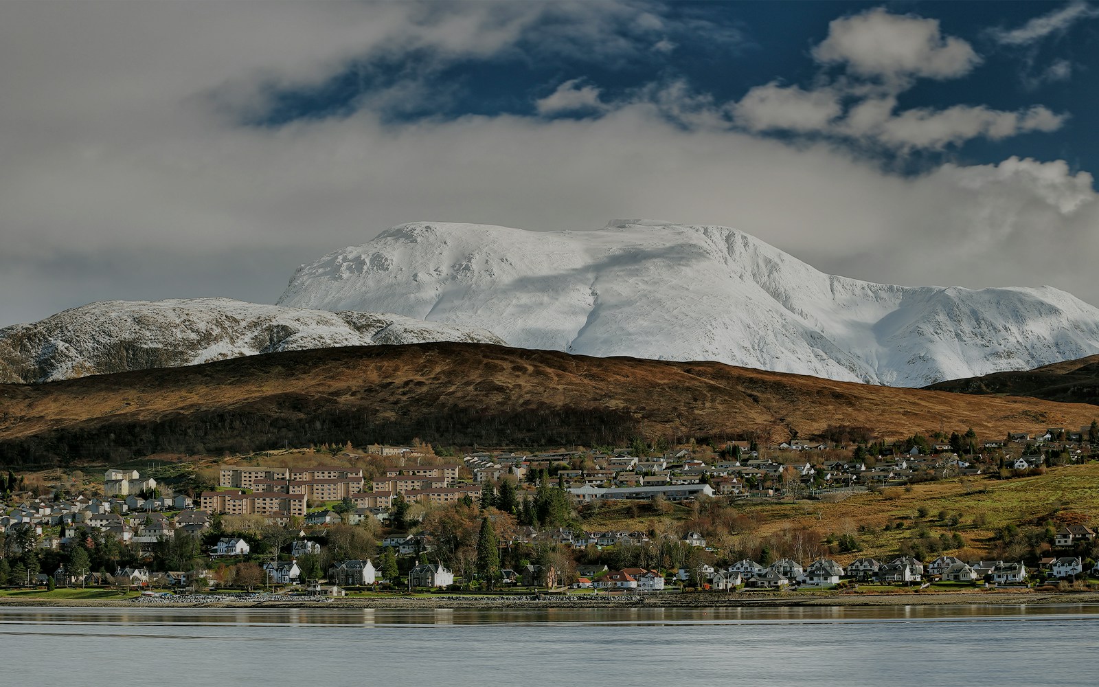 Fort William town with snow-covered Ben Nevis in the background during winter.