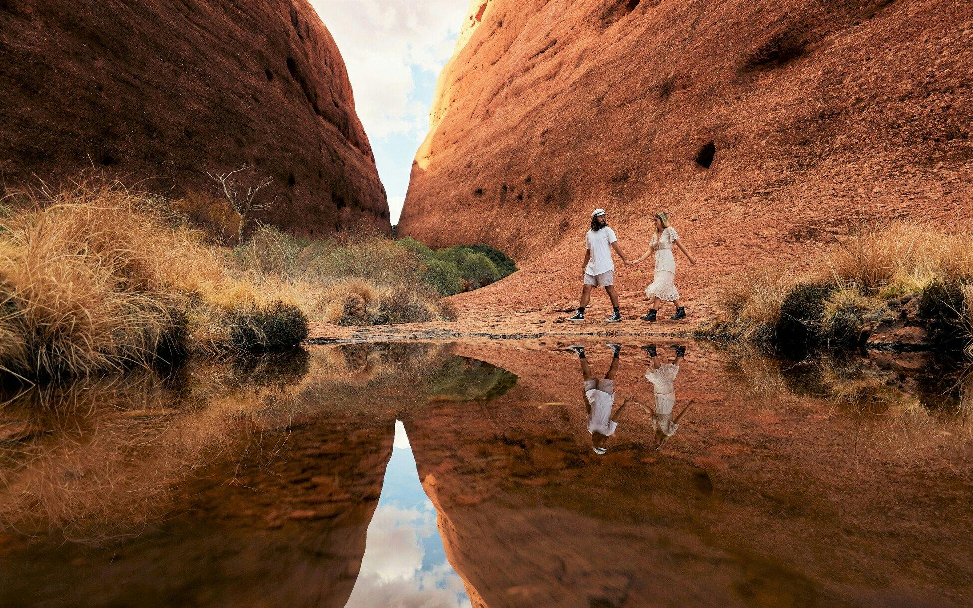 Couple walking through Kata Tjuta rock formations on Uluru Outback camping adventure.