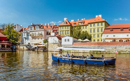 Sightseeing cruise boat on Devils Channel with colorful buildings in Prague.
