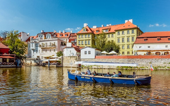 Sightseeing cruise boat on Devils Channel with colorful buildings in Prague.