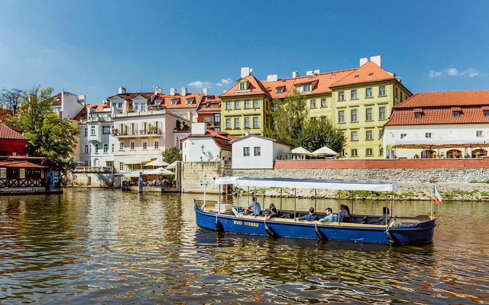 Sightseeing cruise boat navigating Devils Channel in Prague with historic buildings in the background.