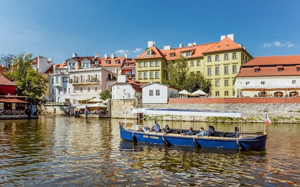 Sightseeing cruise boat on Devils Channel with colorful buildings in Prague.