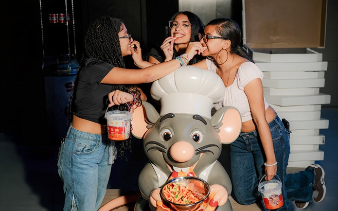 Three people enjoying candy with a chef mouse statue at iCandy Experience in NYC.