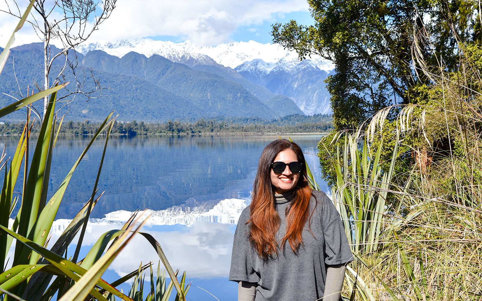 Tourist smiling by Lake Matheson with Southern Alps in background, Franz Josef.