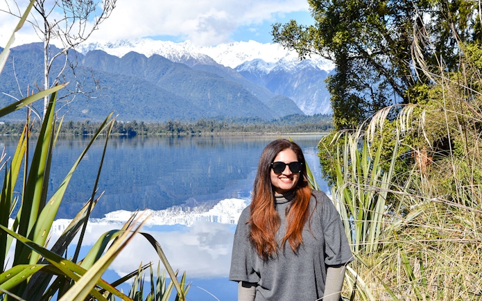 Tourist smiling by Lake Matheson with Southern Alps in background, Franz Josef.