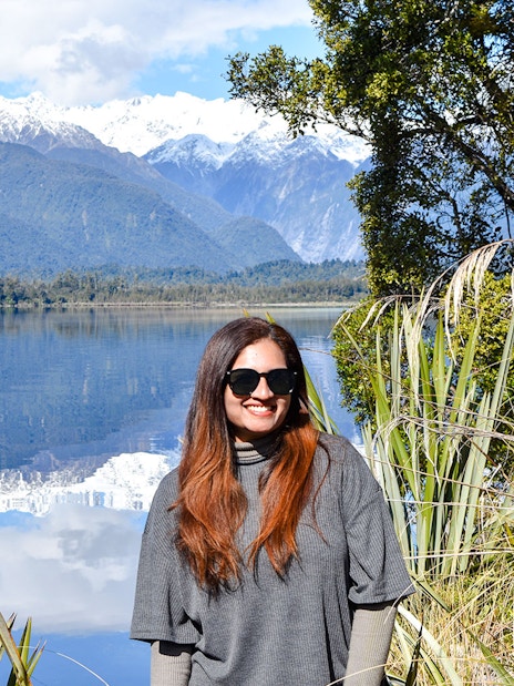 Tourist smiling by Lake Matheson with Southern Alps in background, Franz Josef.