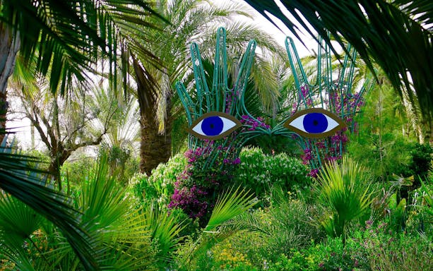 Sculpture with blue eyes among lush greenery at ANIMA Garden.