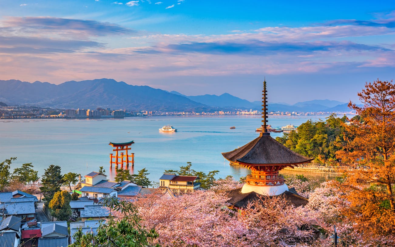 Miyajima Island view with Itsukushima Shrine's torii gate, cherry blossoms, and pagoda, Hiroshima, Japan.