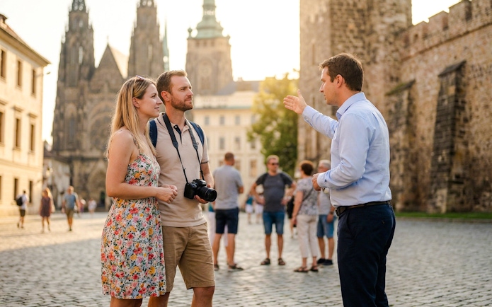 Couple listening to a guide at Prague Castle with cathedral in background.
