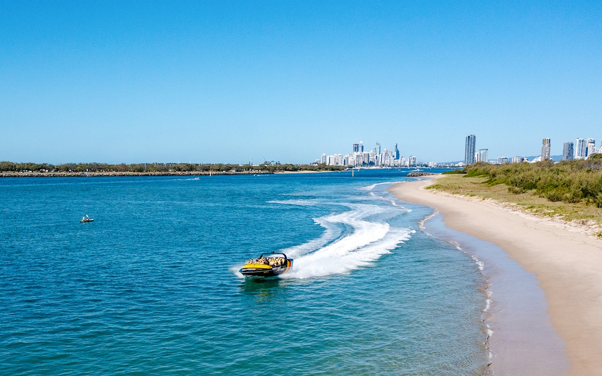 Jet boat speeding along Gold Coast shoreline with city skyline in background.