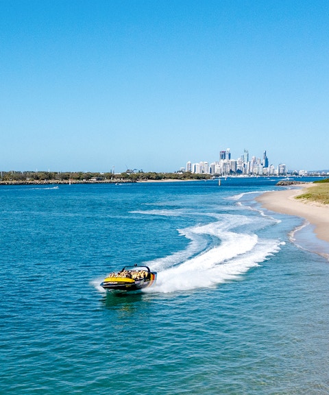 Jet boat speeding along Gold Coast shoreline with city skyline in background.