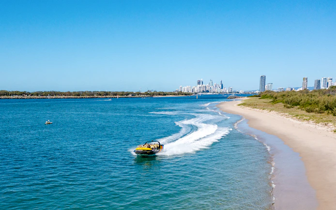 Jet boat speeding along Gold Coast shoreline with city skyline in background.