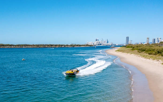 Jet boat speeding along Gold Coast shoreline with city skyline in background.