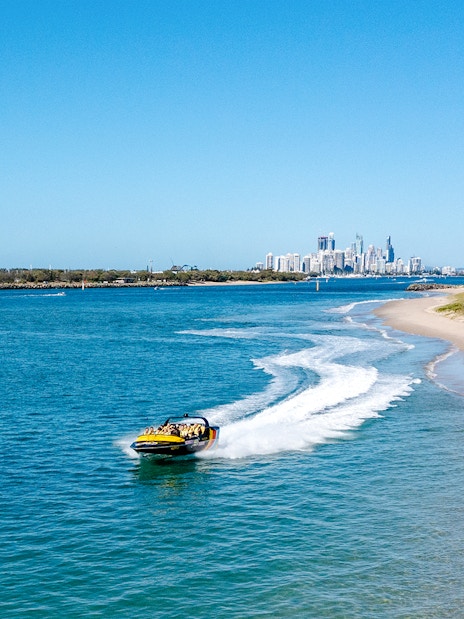 Jet boat speeding along Gold Coast shoreline with city skyline in background.