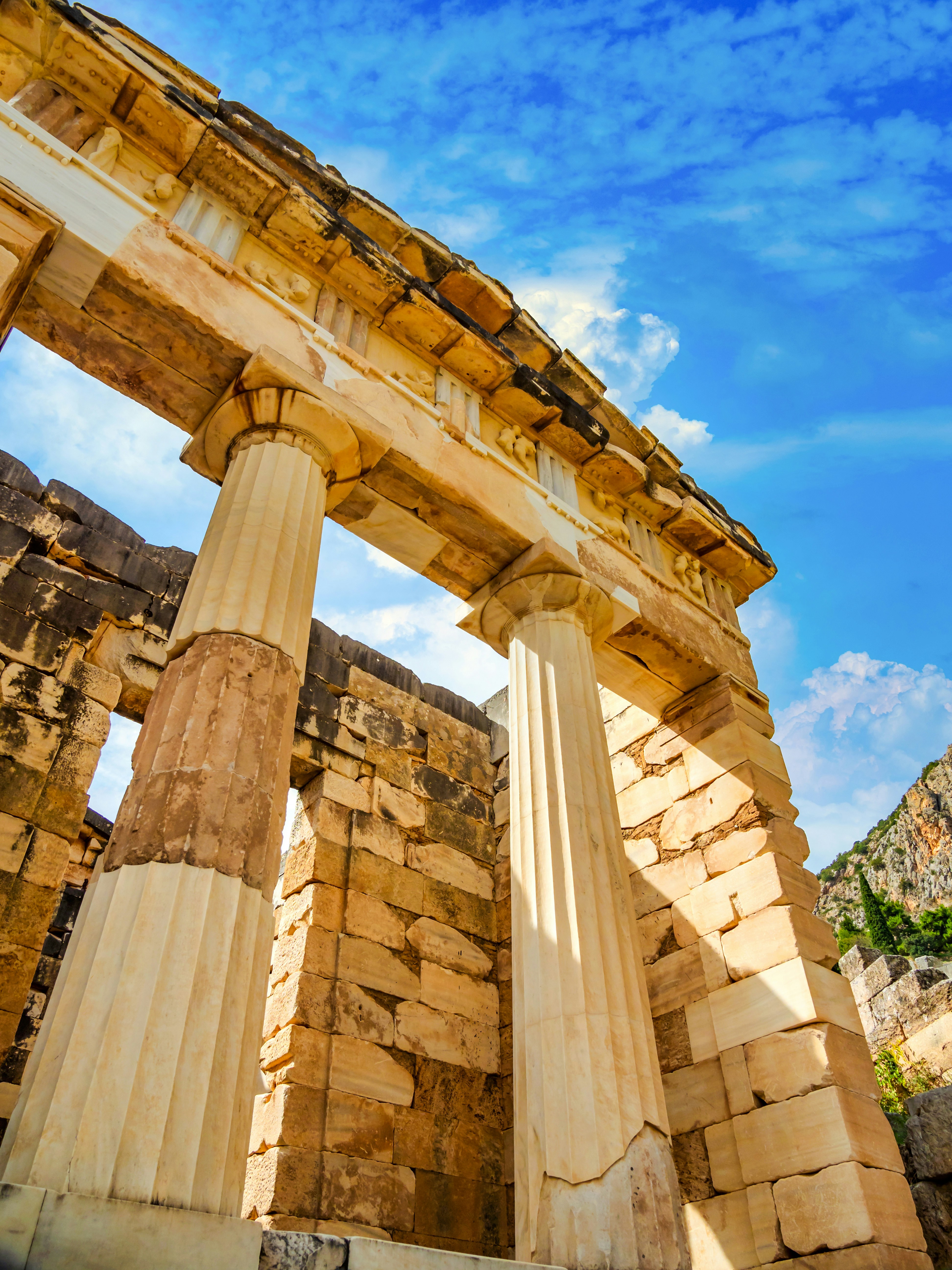 Athenian Treasury columns and stone structure under a blue sky at Delphi, Greece.