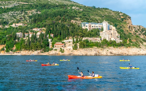 Kayakers paddling near Dubrovnik's coastline with lush hills in the background.