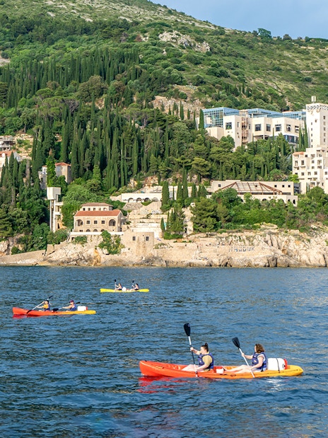 Kayakers paddling near Dubrovnik's coastline with lush hills in the background.