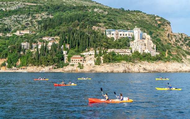 Kayakers paddling near Dubrovnik's coastline with lush hills in the background.