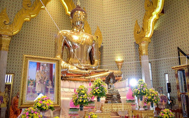 Golden Buddha statue at Wat Traimit, Bangkok, surrounded by floral arrangements.
