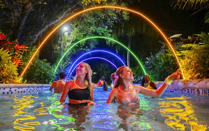 Guests enjoying AquaGlow event at Aquatica San Antonio under colorful illuminated arches.