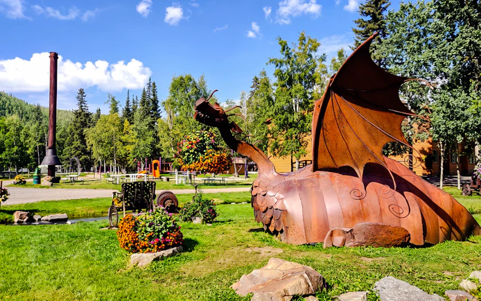 Metal dragon sculpture at Chena Hot Springs with surrounding greenery and picnic area.